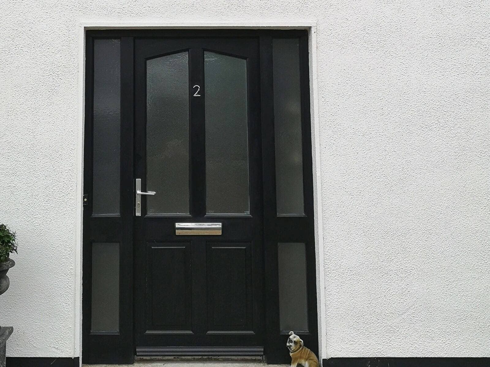 Dunkle Kunststoff-Haustür mit Seitenteilen und Briefeinwurf an einem verputzten Wohnhaus